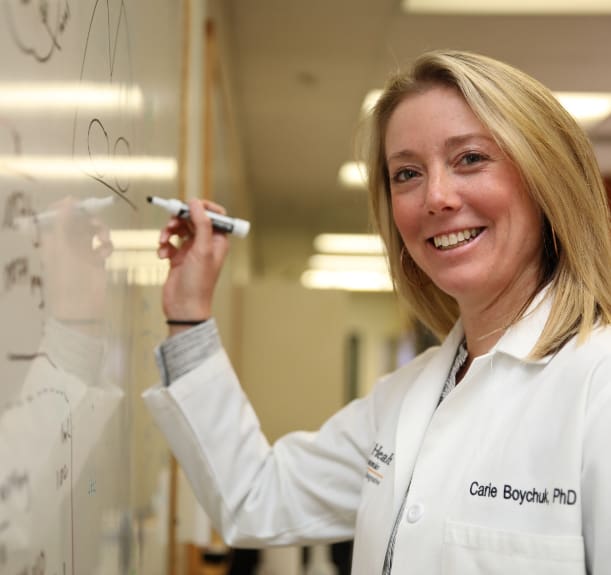 Dr. Boychuk writes mathematical equation on lab white board.